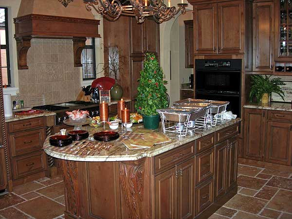 Kitchen with dark wood cabinets, granite countertops, large island with serving dishes, and a decorative range hood.