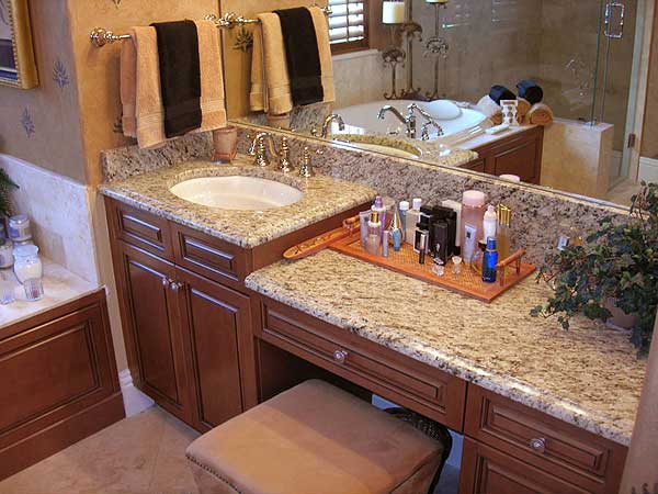 Bathroom vanity with granite countertop, undermount sink, and wood cabinetry. Bathtub visible in background.