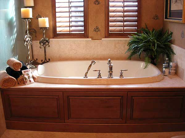 Bathroom with oval soaking tub, wood cabinetry, marble tile, and plantation shutters.