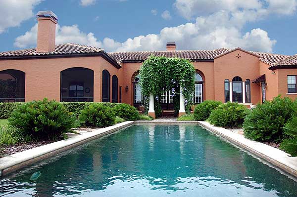 House plan exterior, Mediterranean style, single-story with arched windows, tiled roof, prominent chimney, and covered entry.