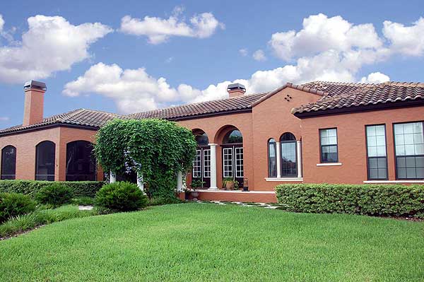 House plan exterior with arched windows, tile roof, prominent chimney, and covered arched entryway supported by columns.