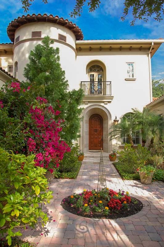 Mediterranean style house plan exterior with curved tower, arched entryway, wrought iron balcony, and tile roof.