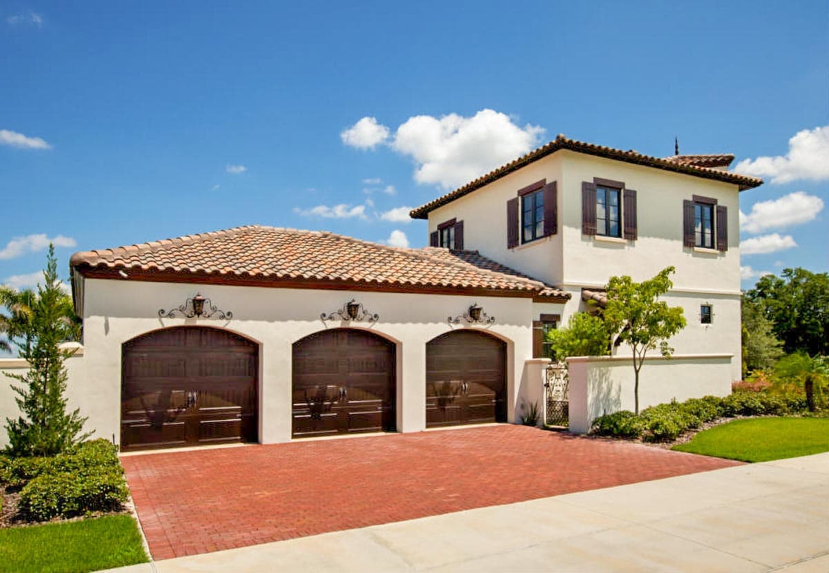 House plan exterior featuring a three-car garage, tile roof, stucco walls, and arched garage doors.