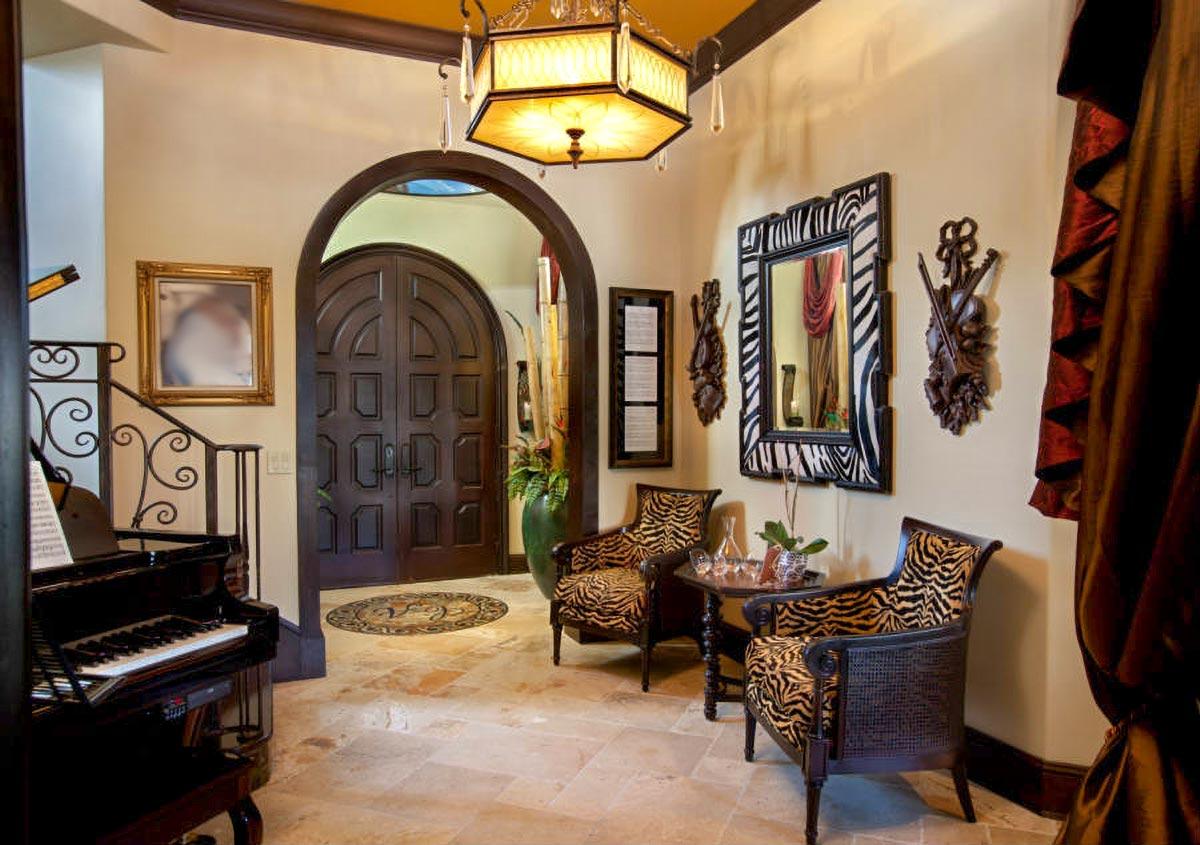 Foyer interior with grand arched double doors, stone flooring, a grand piano, seating area, and decorative mirror.