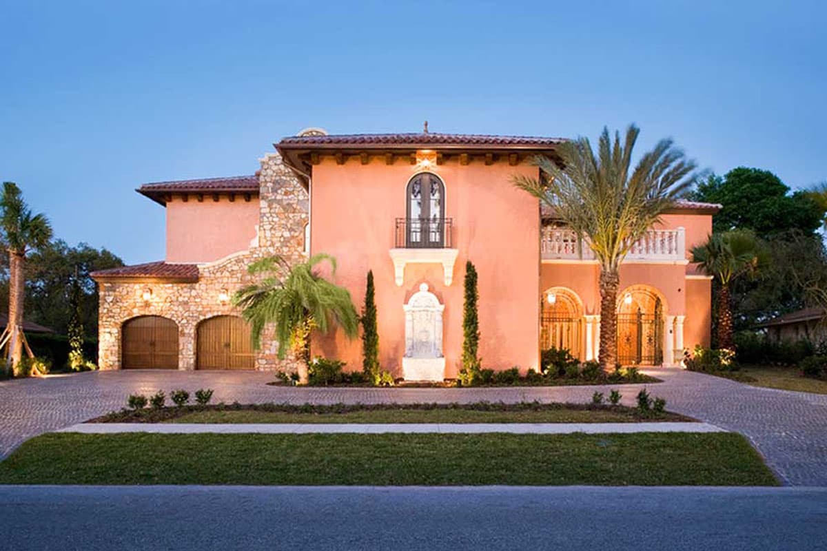 Mediterranean-style house plan exterior with stucco facade, stone accents, dual garage doors, second-story balcony, and arched entryway.