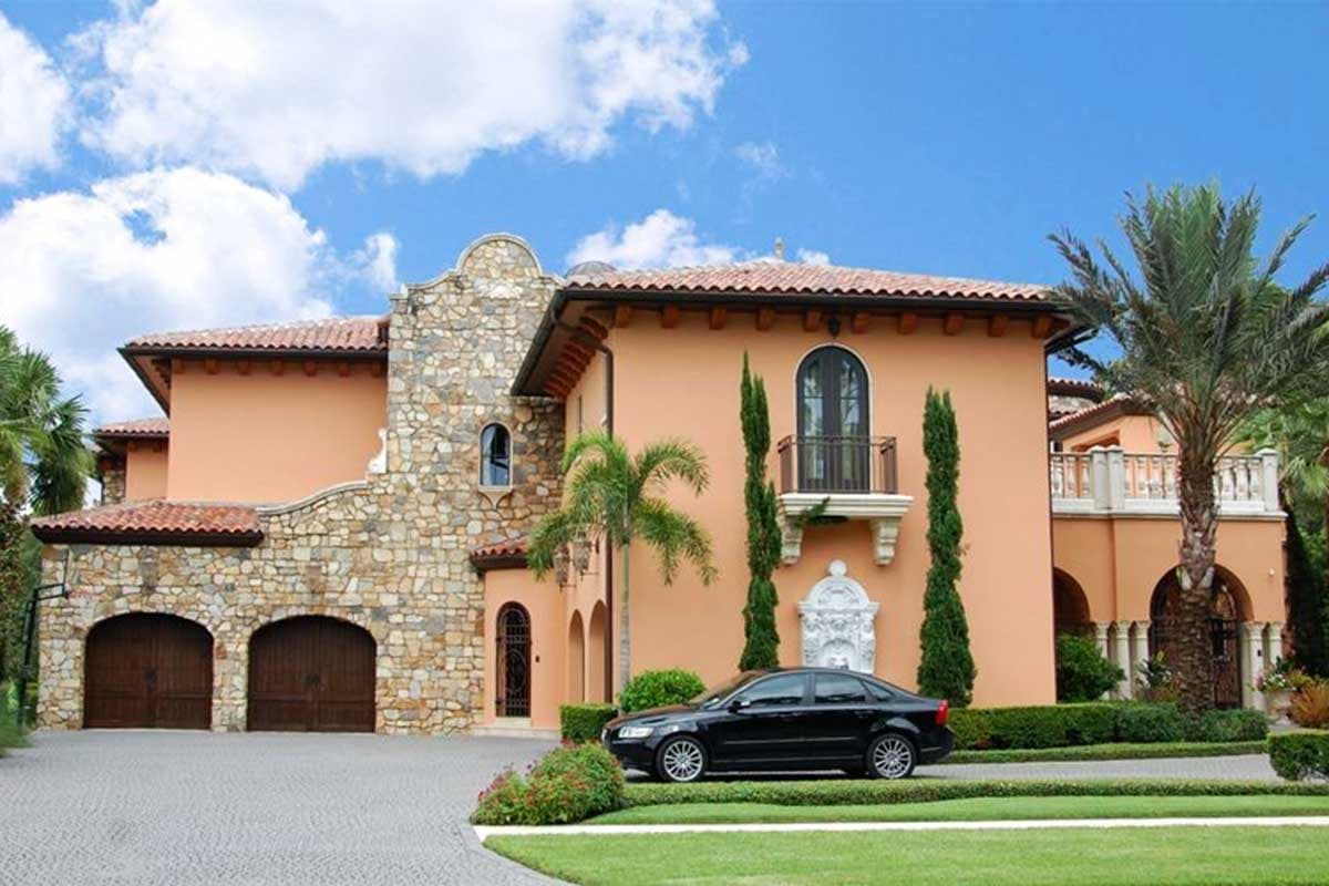 Mediterranean style house plan exterior with stone facade, arched garage doors, balcony, and tile roof.