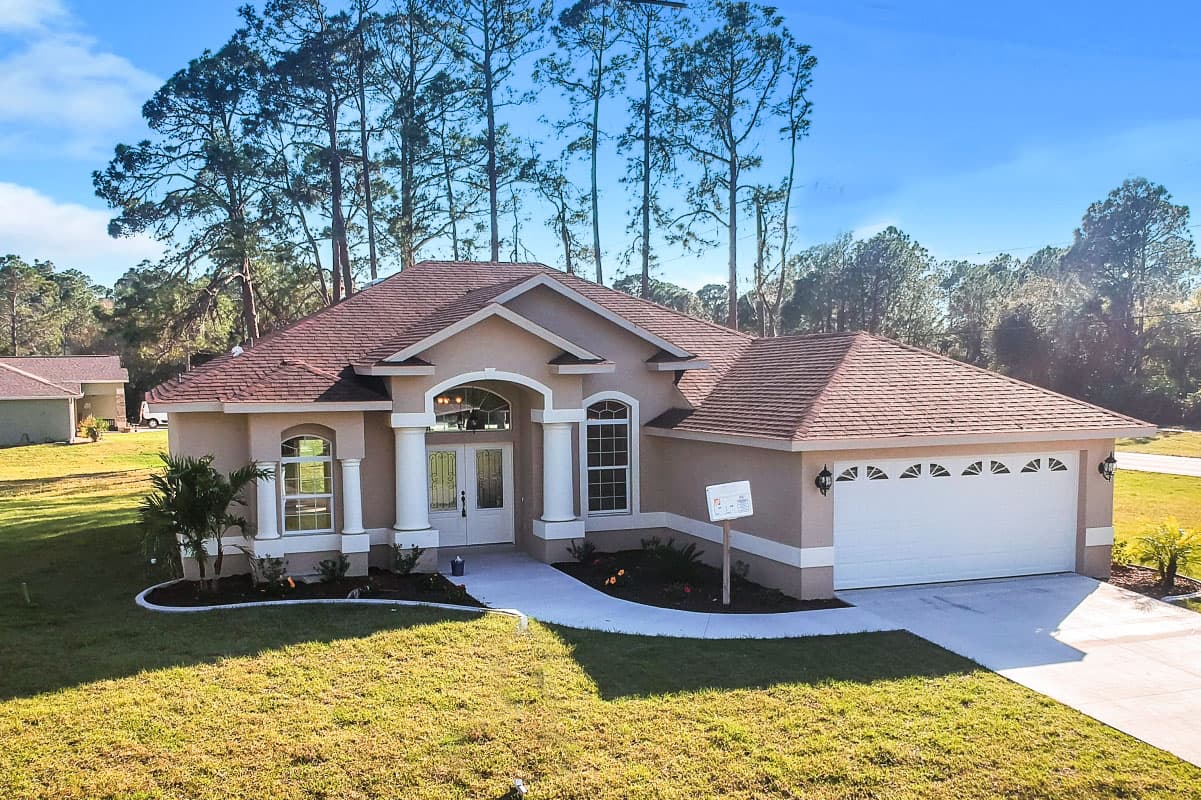 House plan exterior. Ranch style, single-story home with columns flanking the entrance, a hip roof, and a two-car garage.