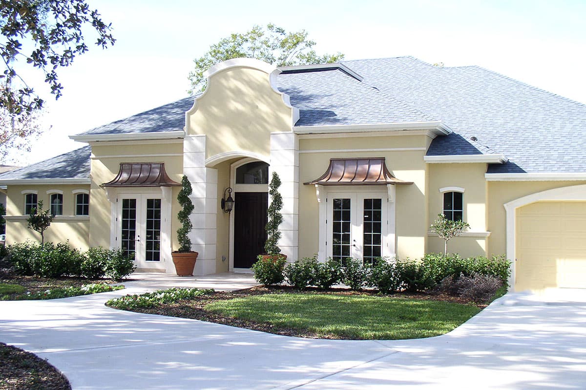 House plan exterior with arched entry, stucco finish, double doors, copper awnings, and attached garage.
