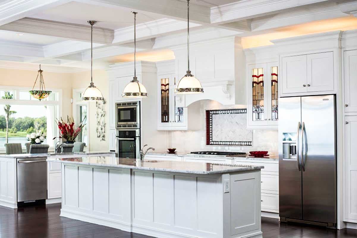 Interior view: White kitchen with large island, stainless steel appliances, coffered ceiling, and pendant lighting.