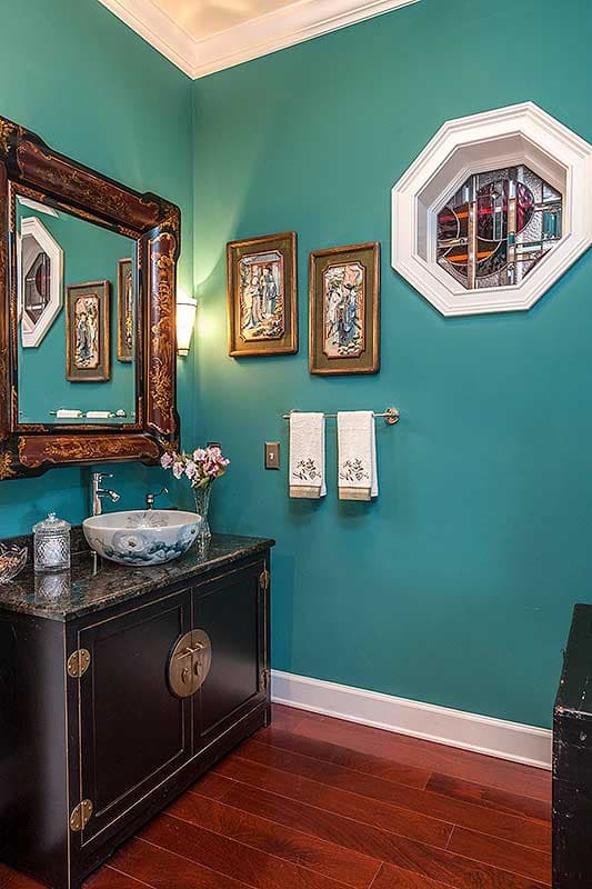 Powder room with teal walls, ornate mirror, decorative vanity, bowl sink, and octagonal stained glass window.