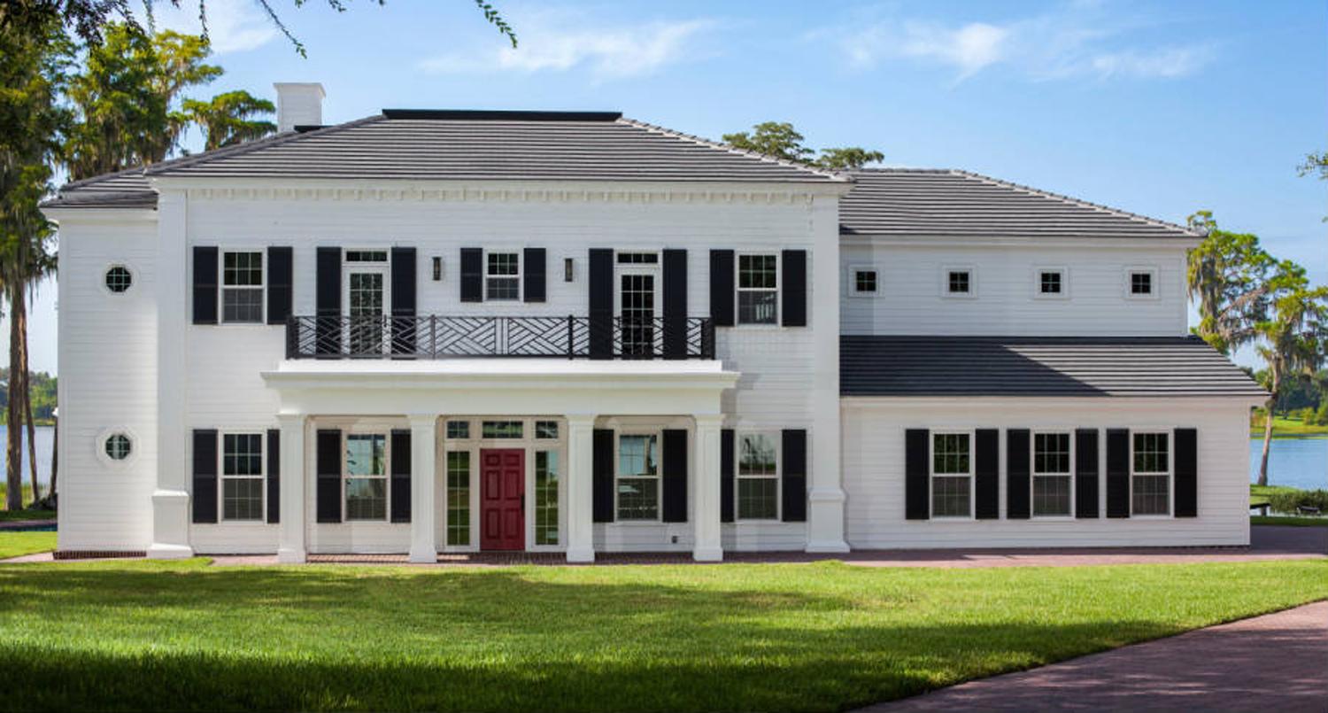 House plan exterior: Two-story white house with a central porch, second-story balcony, dark shutters, and a hip roof.