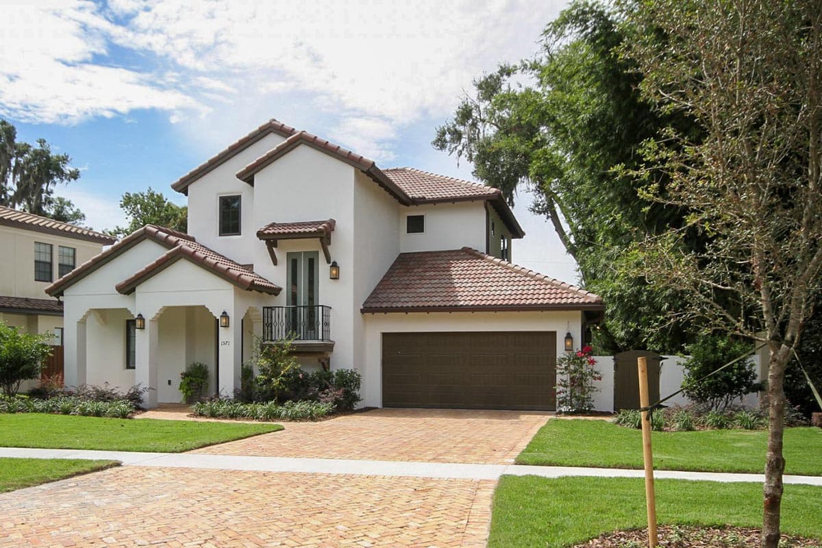House plan exterior. Two-story stucco house with a tile roof. Features include a front porch, balcony, and attached garage.