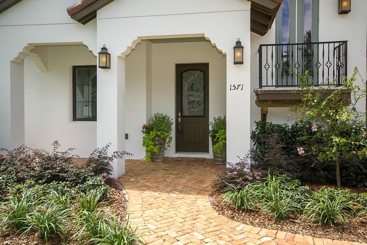 House plan exterior with arched entryway, decorative balcony railing, and tiled walkway.