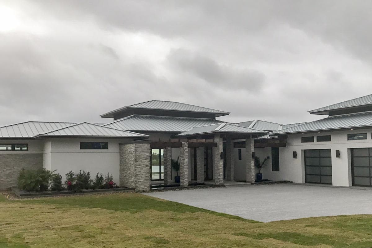 Modern house plan exterior with multi-level metal roofs, stone accents, and a three-car garage with glass doors.