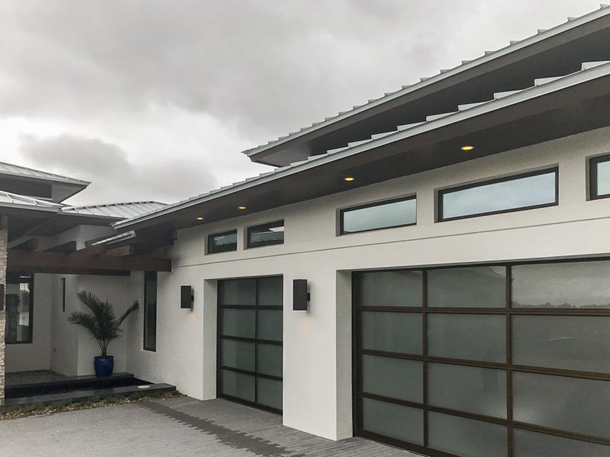 Modern house exterior with metal roof, stacked windows, and frosted glass garage doors.