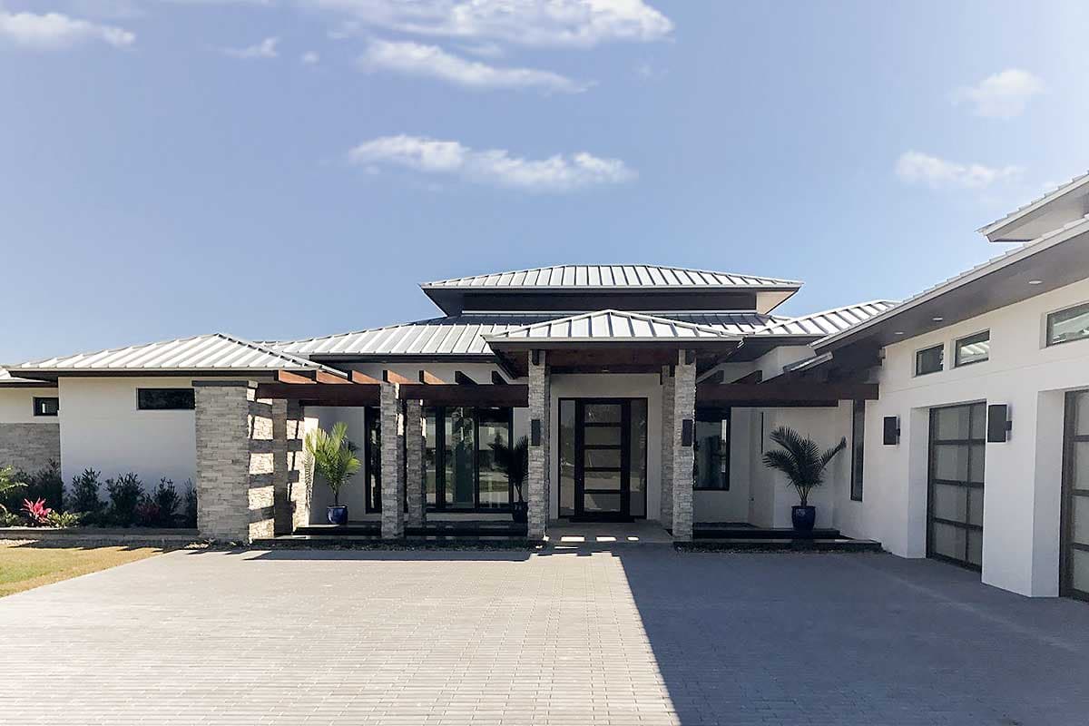 Modern house plan exterior with a multi-level metal roof, stone pillars, and expansive glass doors.