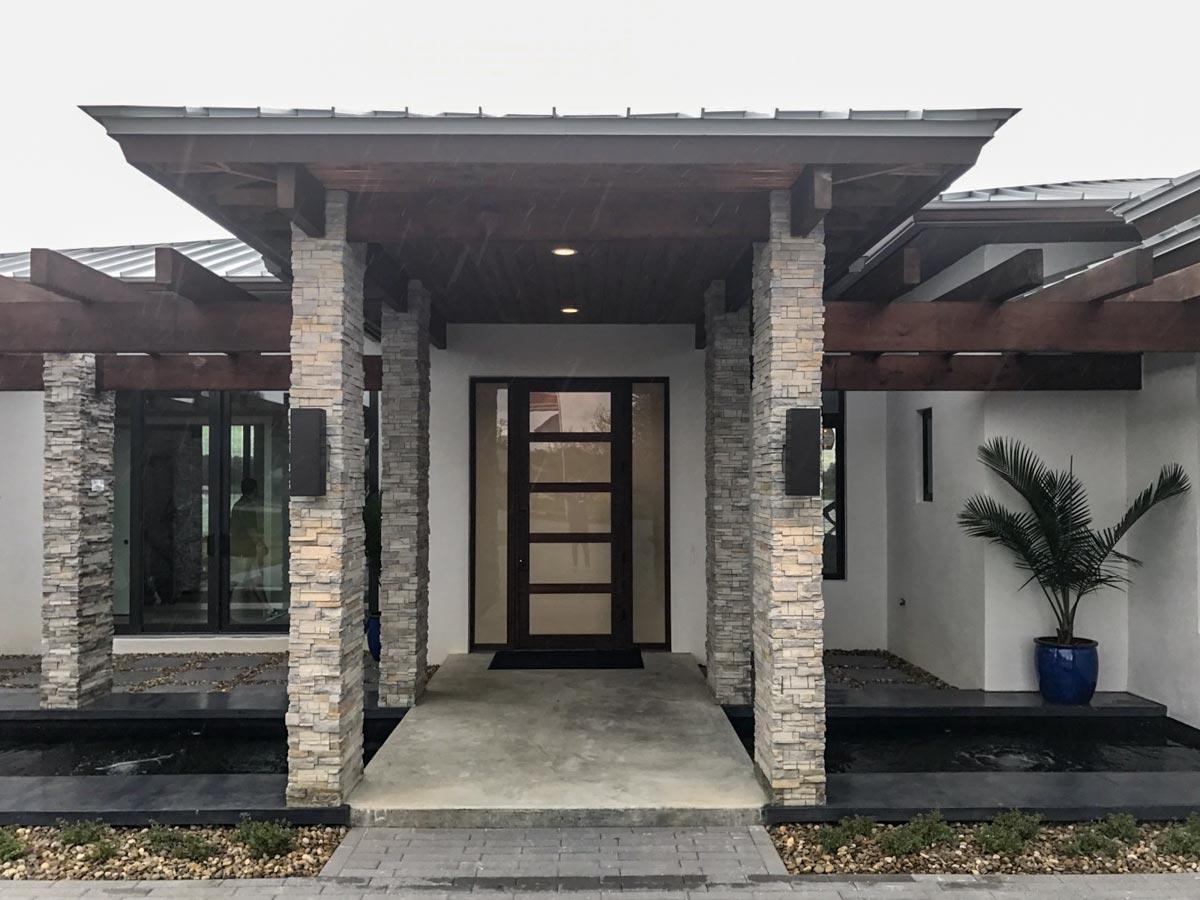Modern house plan exterior with stone-clad columns, wood pergola, and glass-paneled entry door.