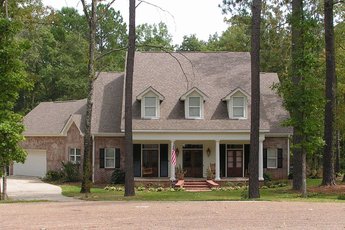 House plan exterior: Two-story brick home with a covered front porch, central dormers and attached garage.