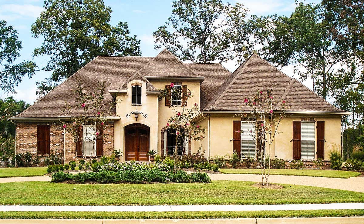 House plan exterior. Two-story home with a gabled roof, brick accents, arched entry, and shuttered windows. Set on a landscaped lot.