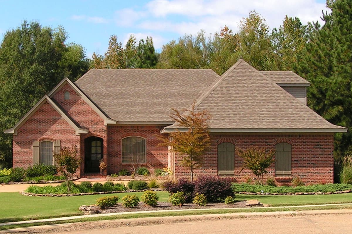 House plan exterior: One-story brick home with prominent gables, arched windows with shutters, and covered entryway.