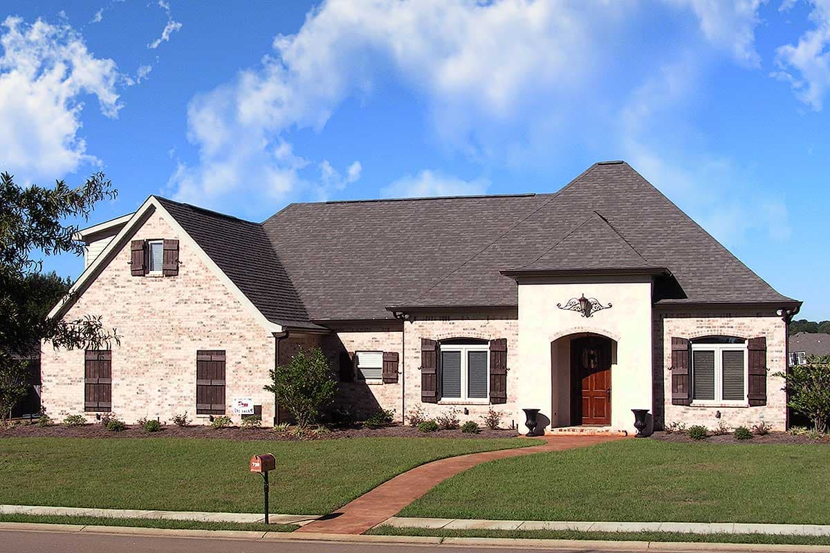 House plan exterior: One-story brick home with arched entryway, dark shutters, and a pitched roofline.