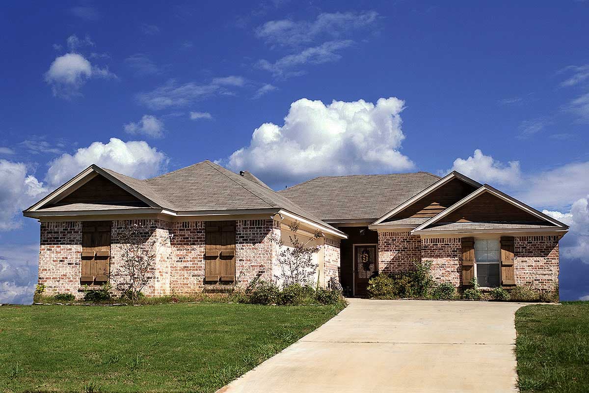 House plan exterior: one-story brick home with gable dormers, wooden shutters, and a side-entry garage.