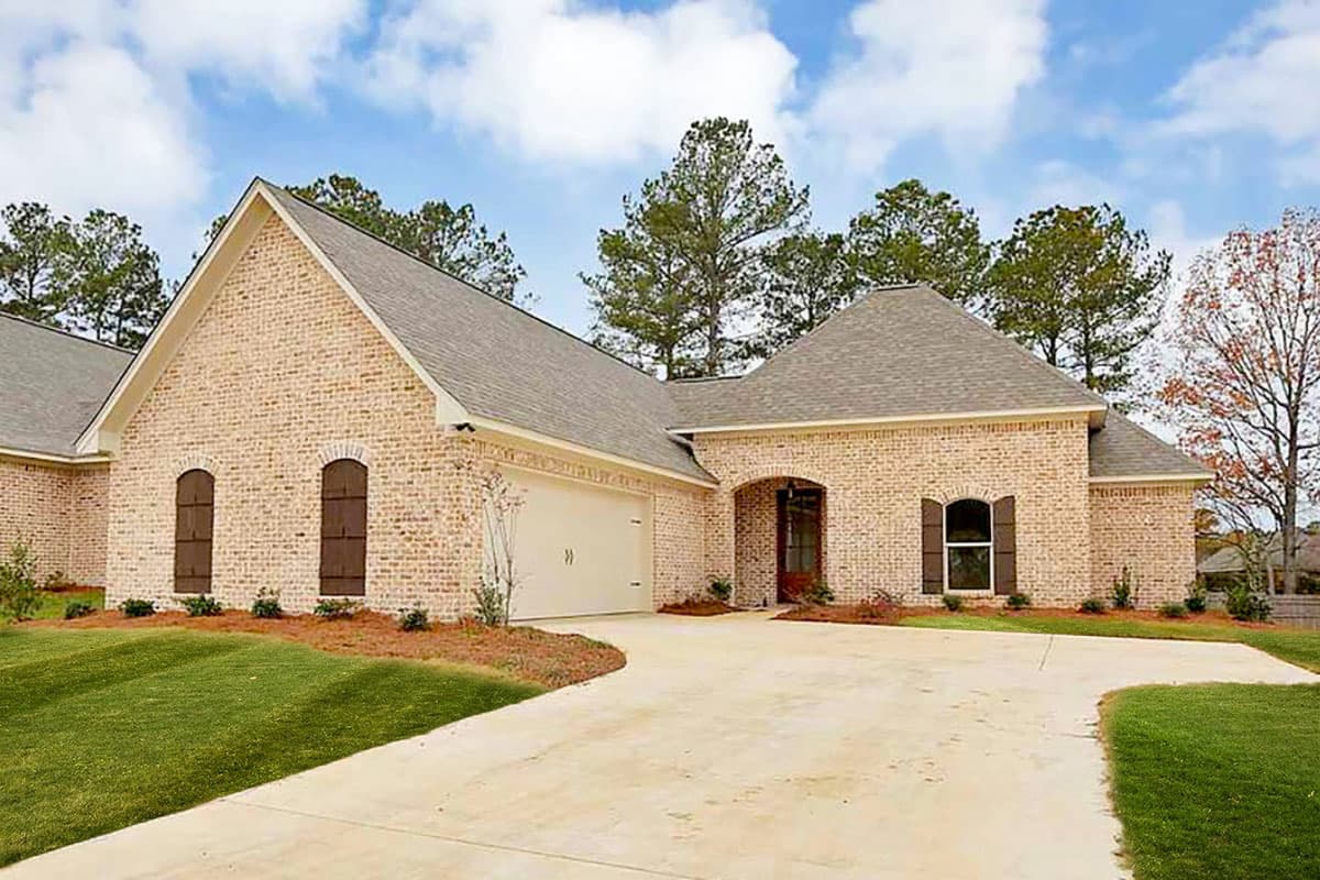 House plan exterior. One-story house with a brick facade. Features include a gabled roof, arched entry, and attached garage. Includes shutters.