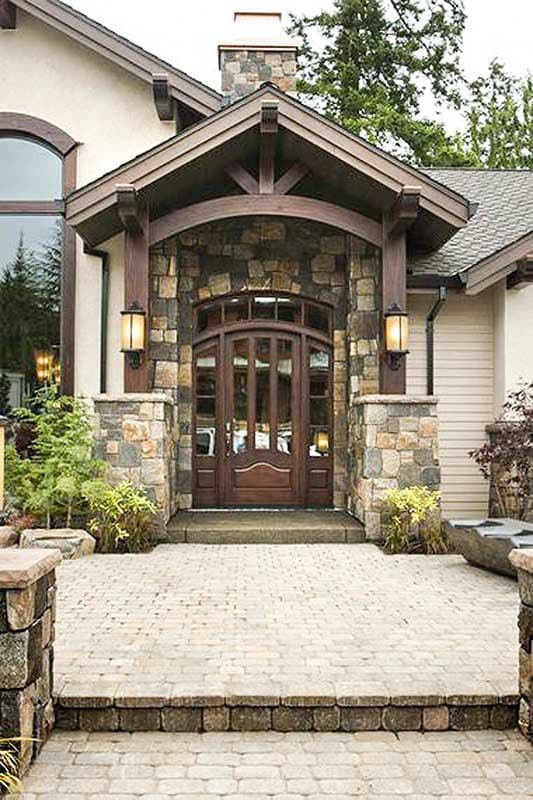 House plan exterior: Covered entry with stone pillars, arched wood doors, timber beams, and multiple gables.