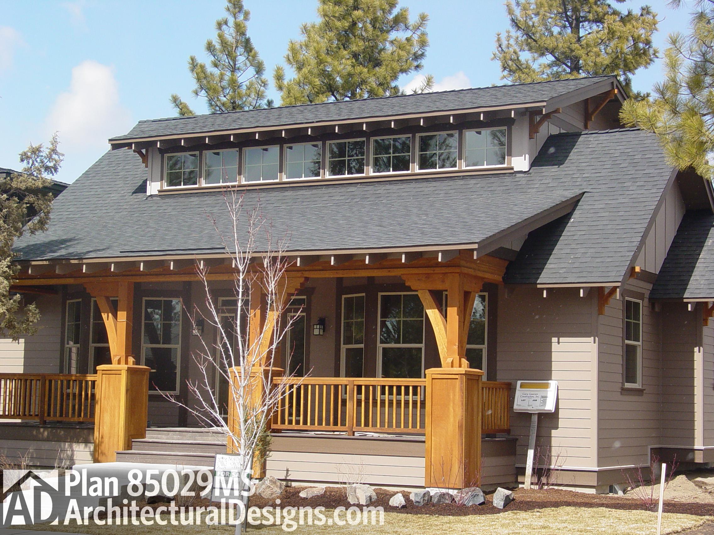 House plan exterior, one story, wide covered porch with timber supports, prominent gable roof, dormer windows.