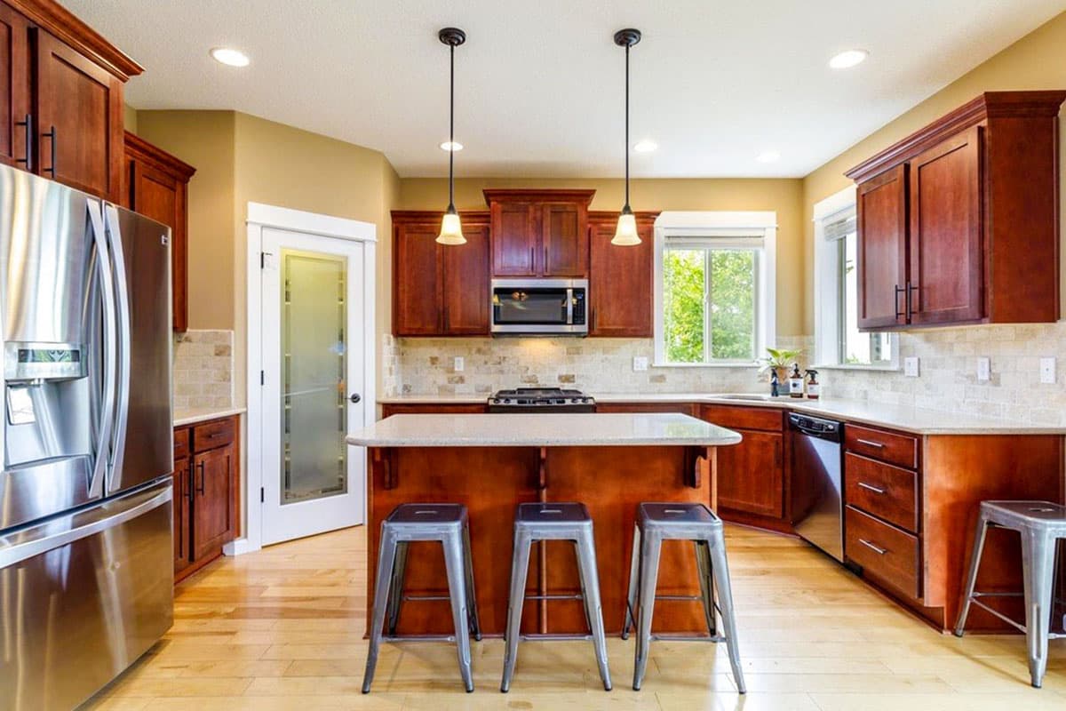 Kitchen with cherry wood cabinets, granite countertops, central island with seating, stainless steel appliances, and a frosted glass door.