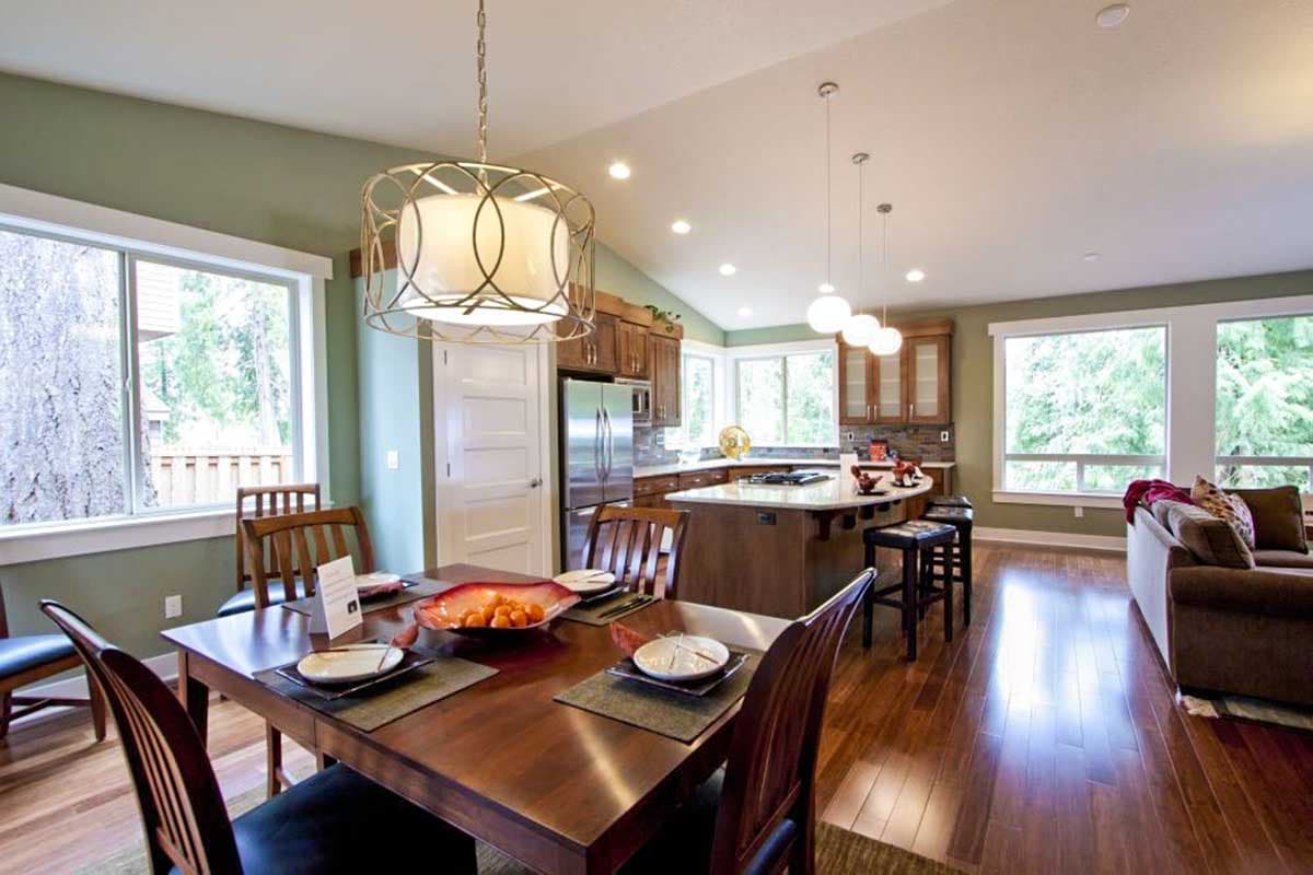 Open-concept dining area and kitchen with vaulted ceiling, island, stainless steel appliances, and large windows.