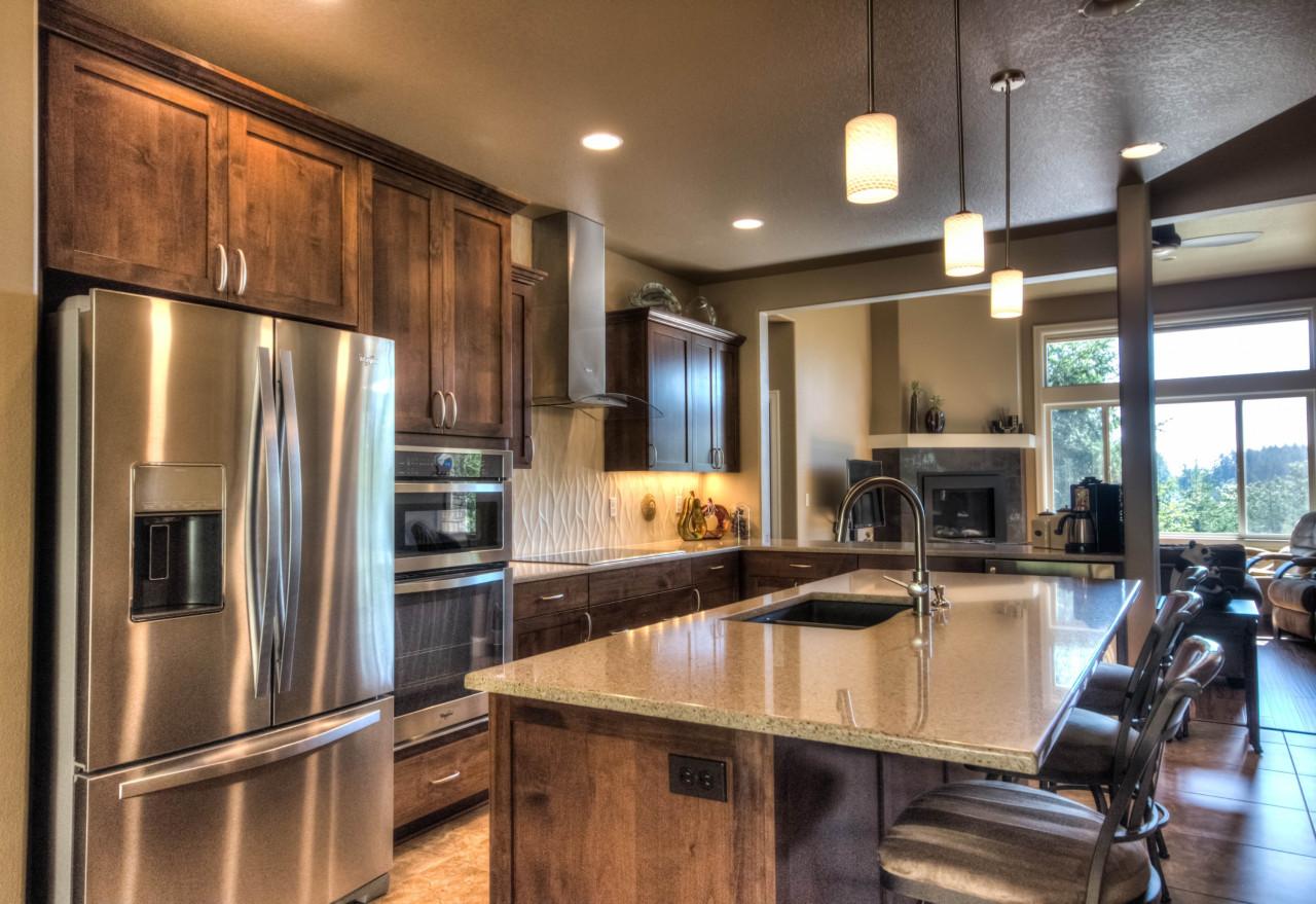 Kitchen with dark wood cabinetry, stainless steel appliances, granite island with sink, and view of living area with fireplace.