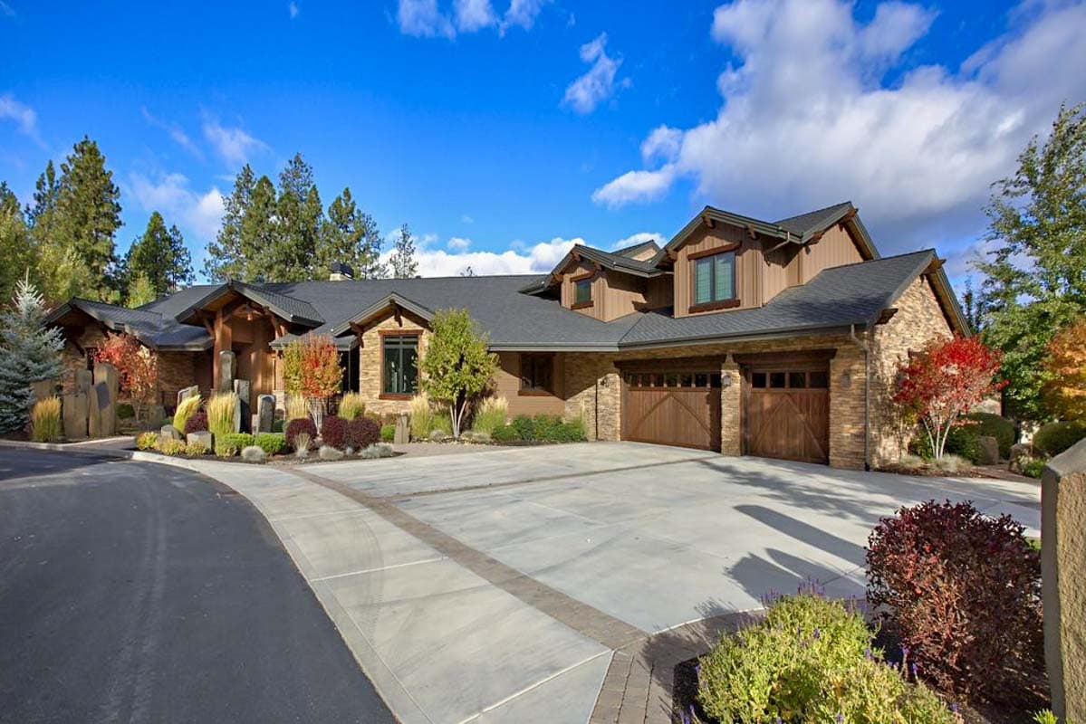 House plan exterior. Two-story, Craftsman style with a gabled roof, stone accents, and three-car garage. Features wood garage doors.