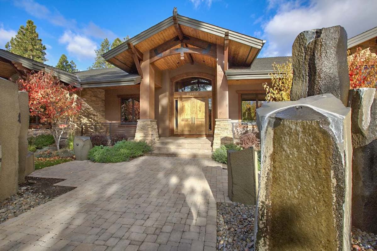House plan exterior with stone accents, double wood doors, deep eaves, and natural stone water feature.