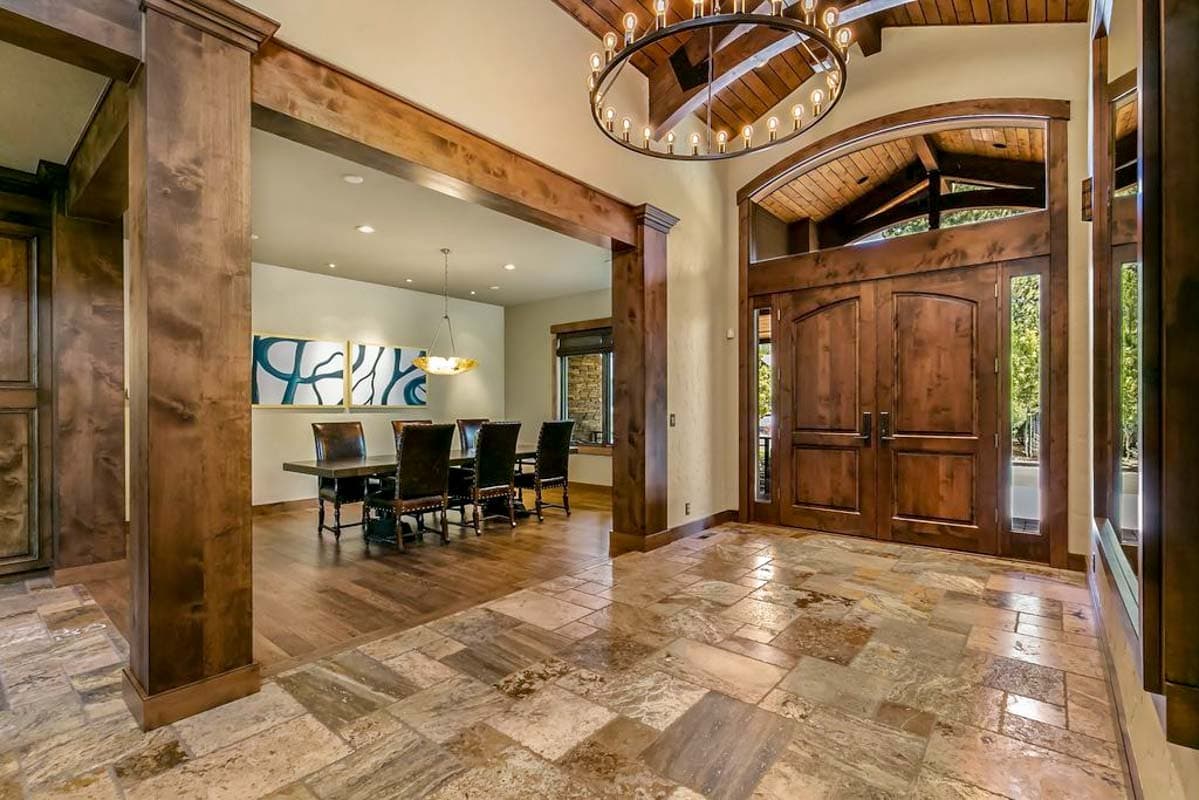 Entrance hall with wood beams, arched double doors, chandelier, and adjacent dining area with table.