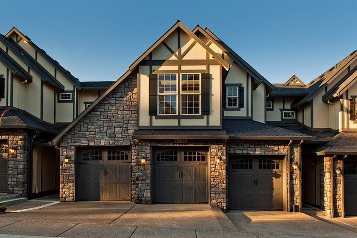 House plan exterior shows a Tudor-style facade with stone lower level, multiple gables, and three garage doors.