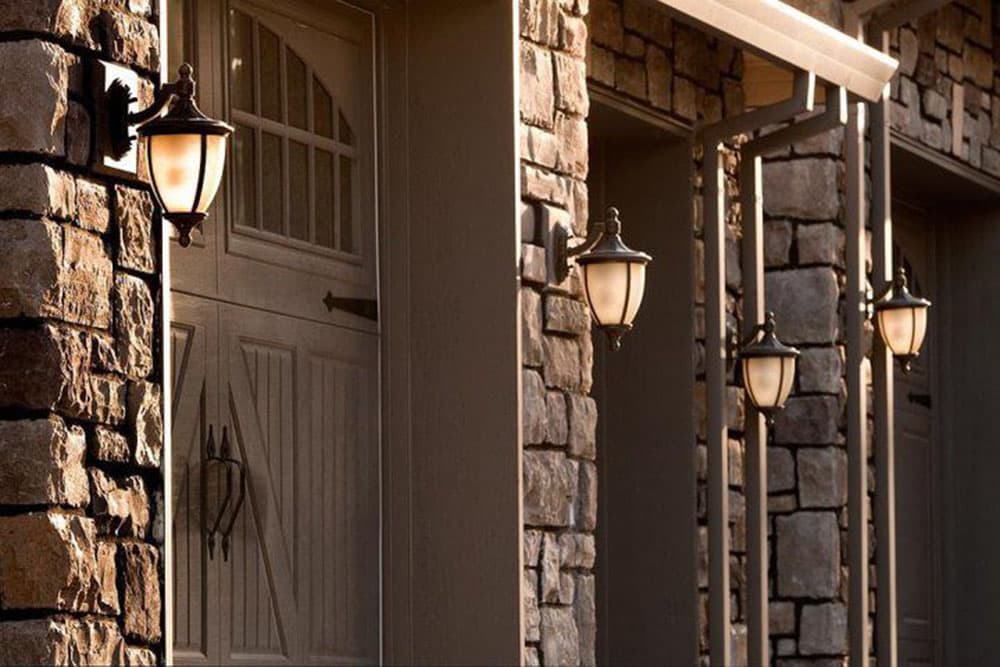 House plan exterior with stone facade, carriage-style garage door, and multiple wall-mounted lantern lights.