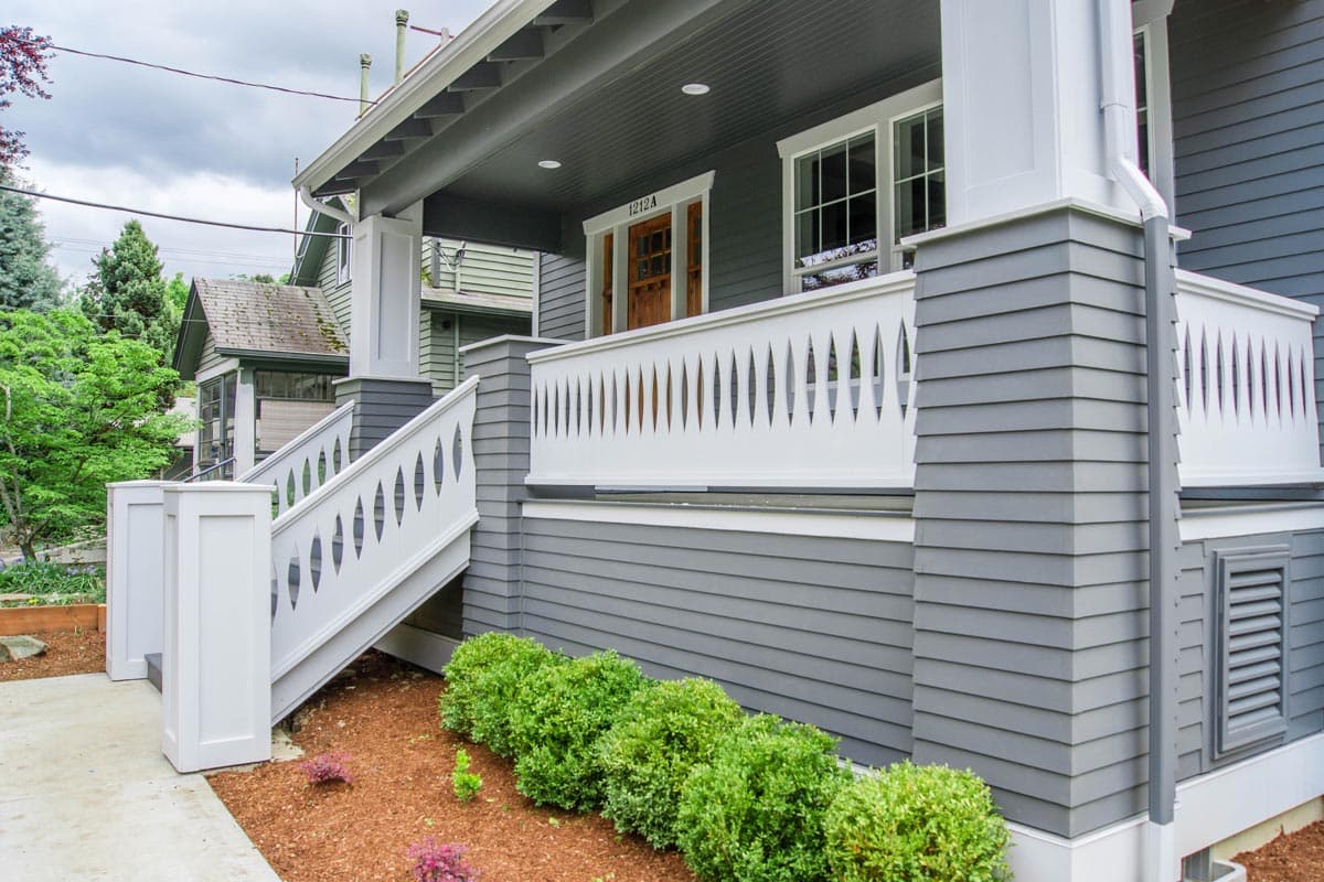 House plan exterior showing a wide porch with a white decorative railing, gray shingle siding, and a set of stairs.