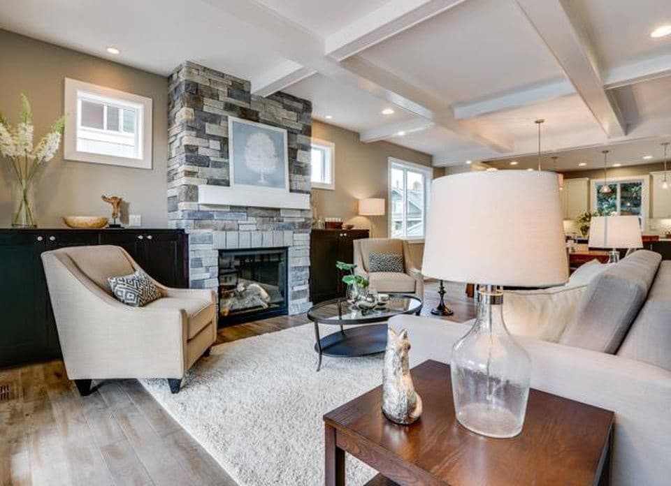 Living room with stone fireplace, coffered ceiling, and open layout leading to kitchen.