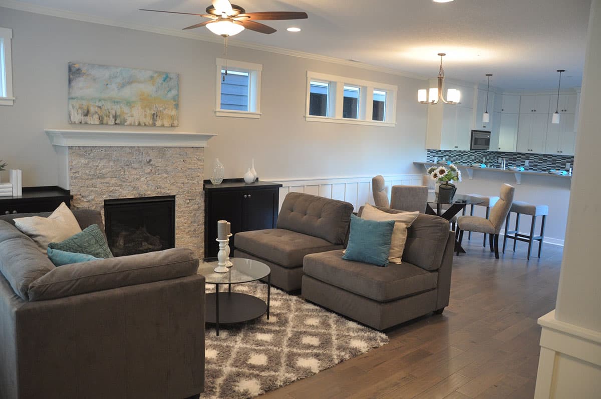 Interior view of a living area with a stacked stone fireplace, sectional sofa, and an open kitchen with a breakfast bar.