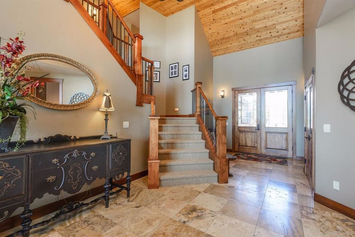 Interior foyer with wood-paneled vaulted ceiling, carpeted stairs, wooden railings, and double entry doors.