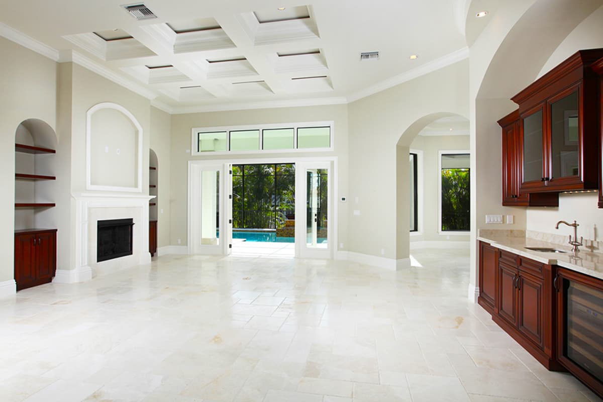 Interior rendering: great room with coffered ceiling, fireplace, built-in shelving, and french doors opening to a pool.