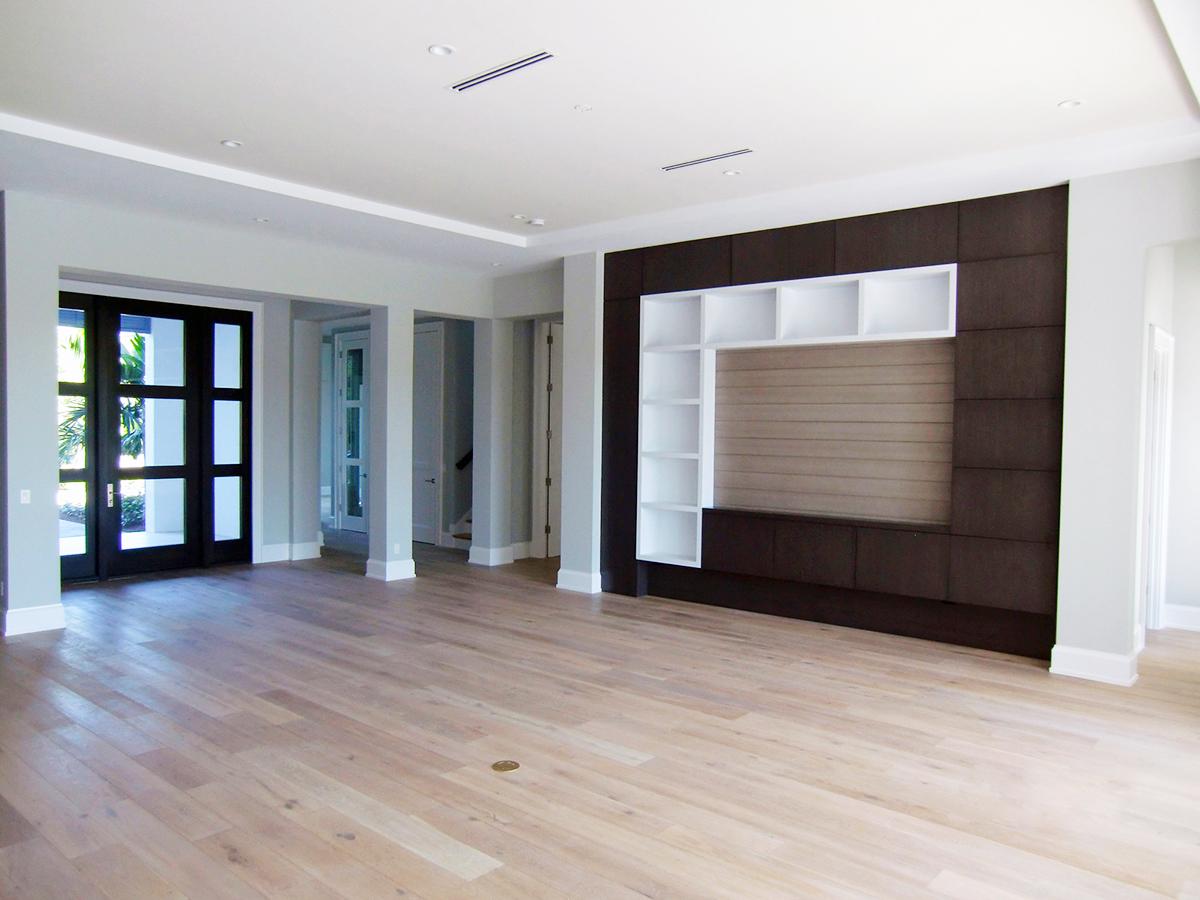 Interior view of a large room with dark wood paneling, white shelving, light wood floors, and double glass doors.