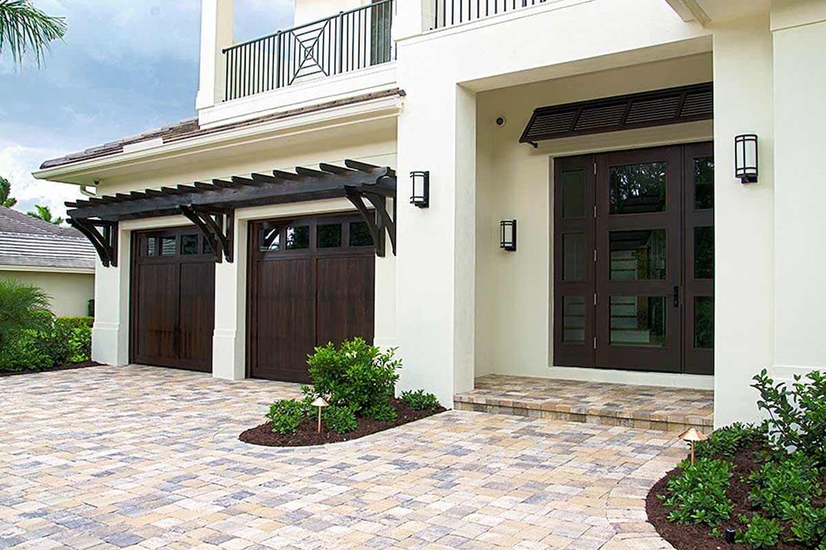 House plan exterior: Two-story home with two-car garage featuring dark wood doors under pergolas and a covered entryway with double glass doors.