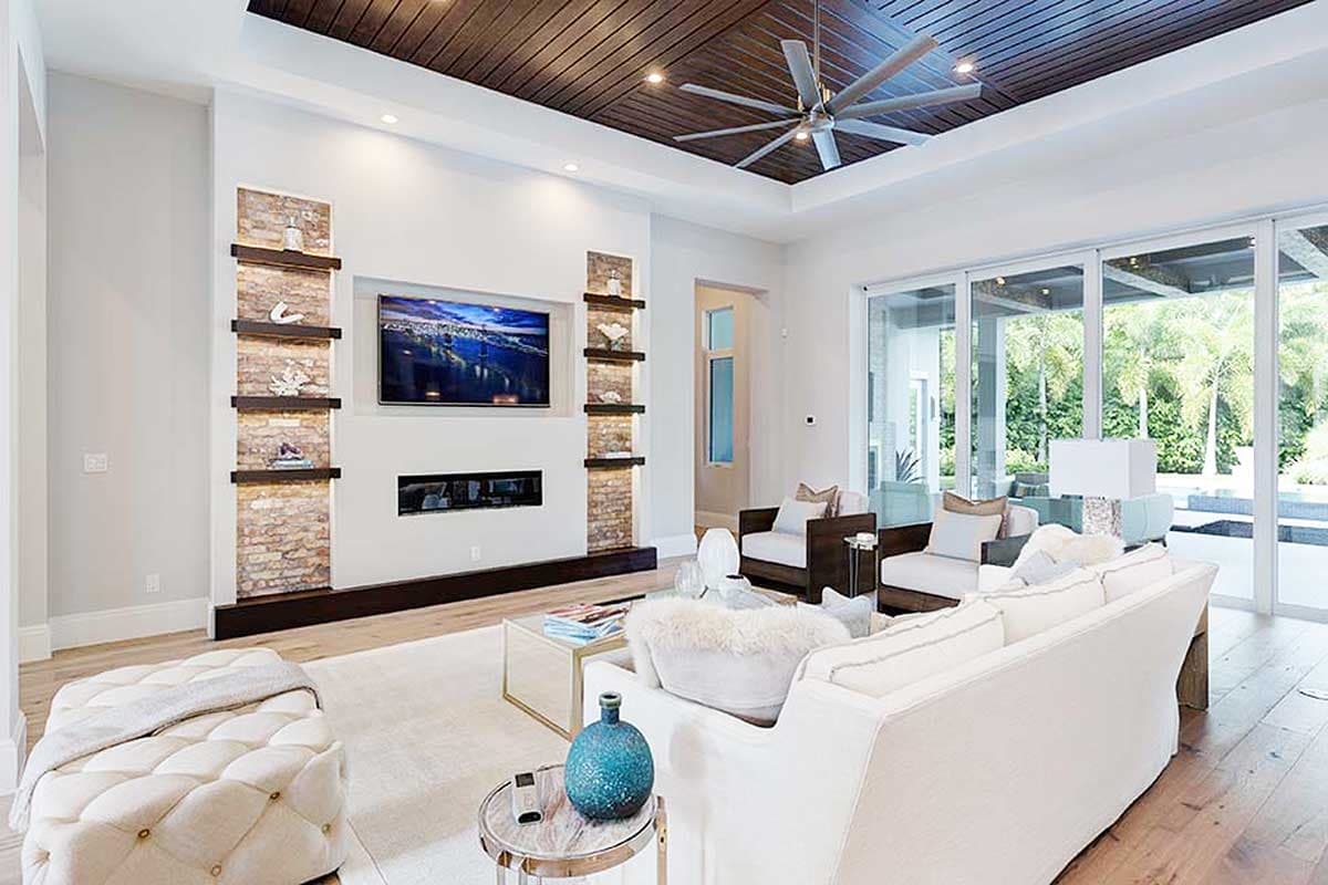 Interior: Living room with fireplace, mounted TV, wood plank ceiling with fan, and large sliding glass doors.