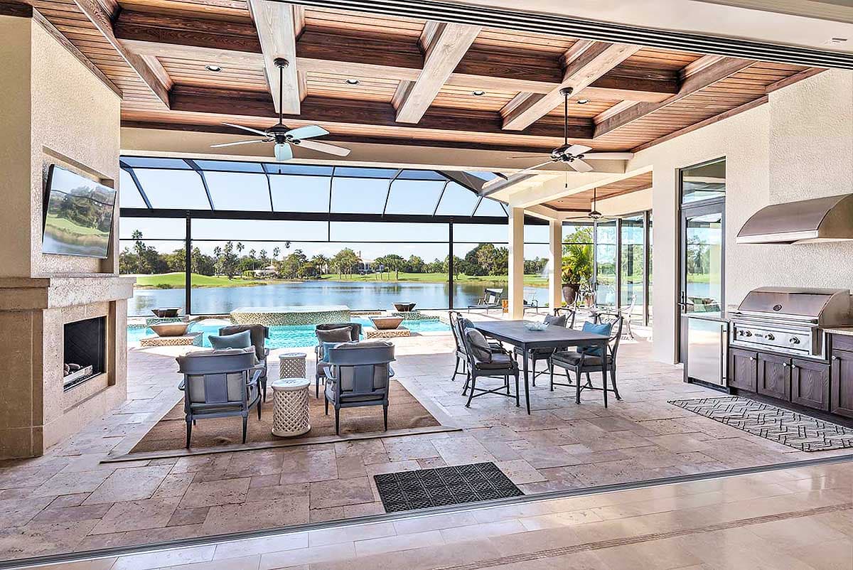 Covered patio with outdoor kitchen, fireplace, seating, dining table, and pool overlooking a golf course.