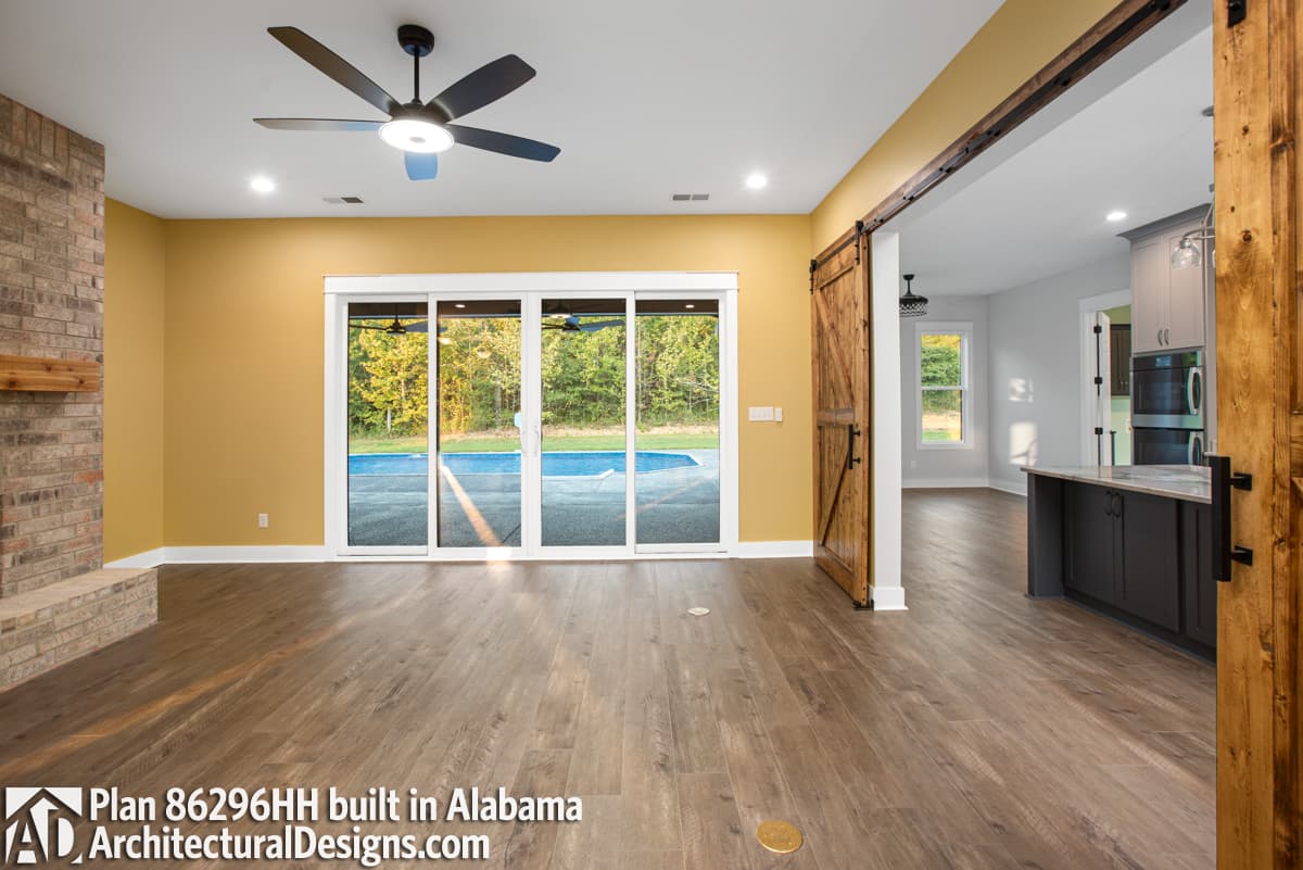 Interior view of a living area with brick fireplace, sliding glass doors to pool, and barn door entry to kitchen.