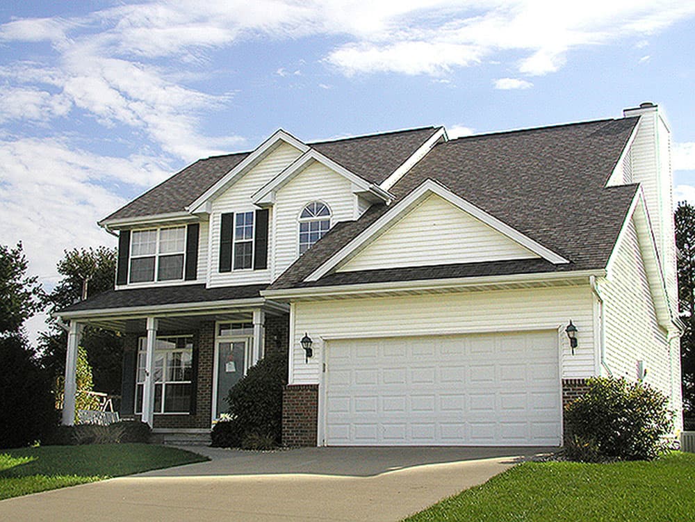 House plan exterior. Two-story home with a gabled roof, front porch, and attached garage. Features include dormers and brick accents.