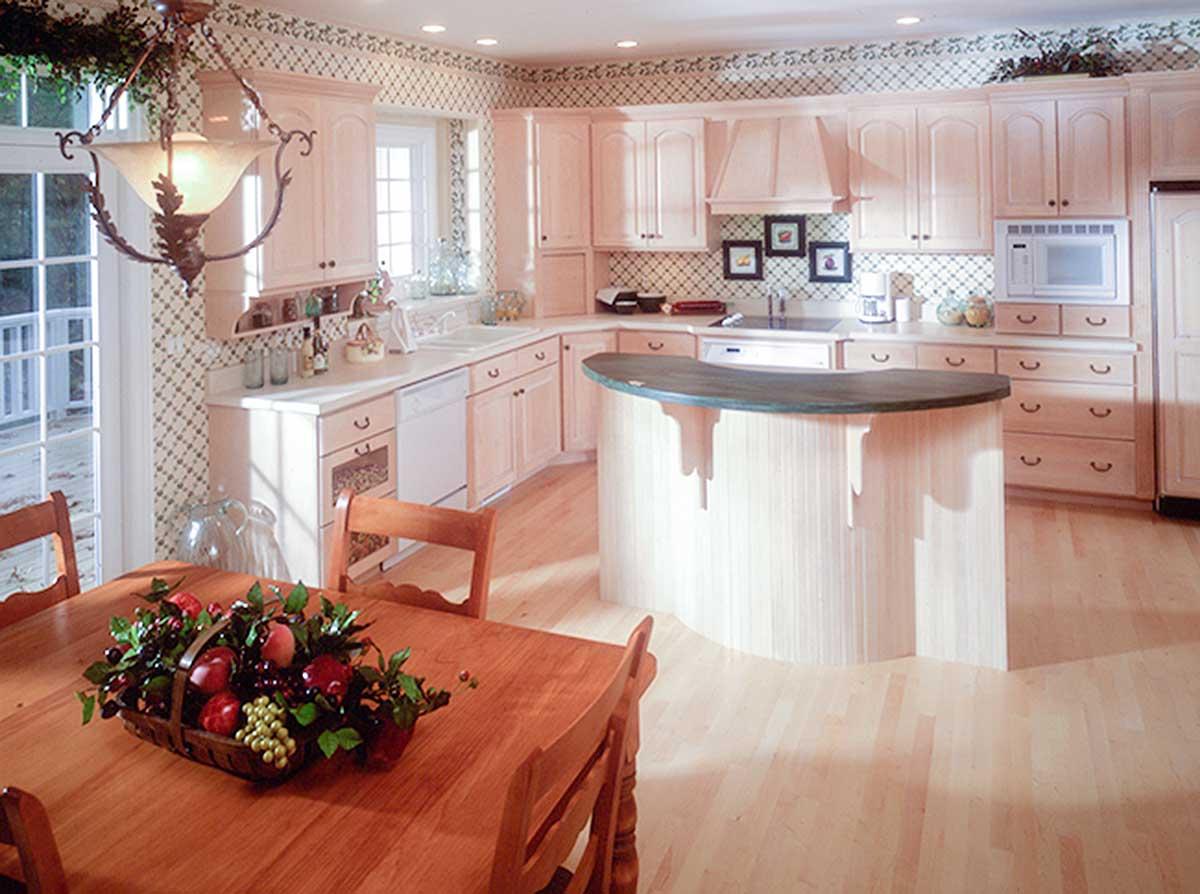Kitchen with light wood cabinets, a curved island with dark countertop, dual sink, and dining table with fruit basket.