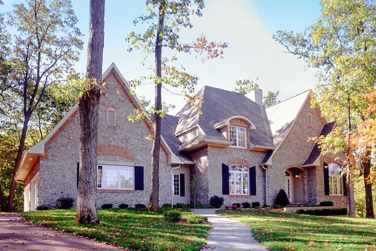 House plan exterior featuring stone facade, multiple gables, dormers, and arched windows.